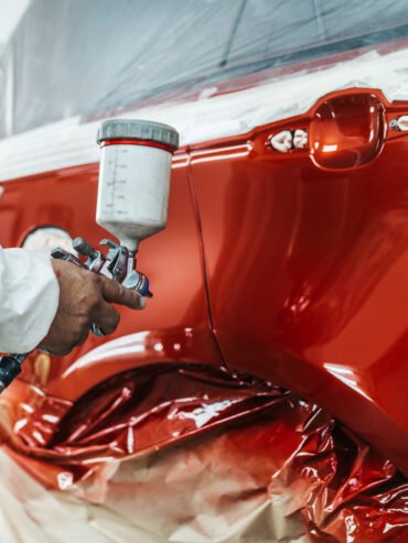 Skilled mechanic applying fresh paint to a car’s surface during a professional paint job.